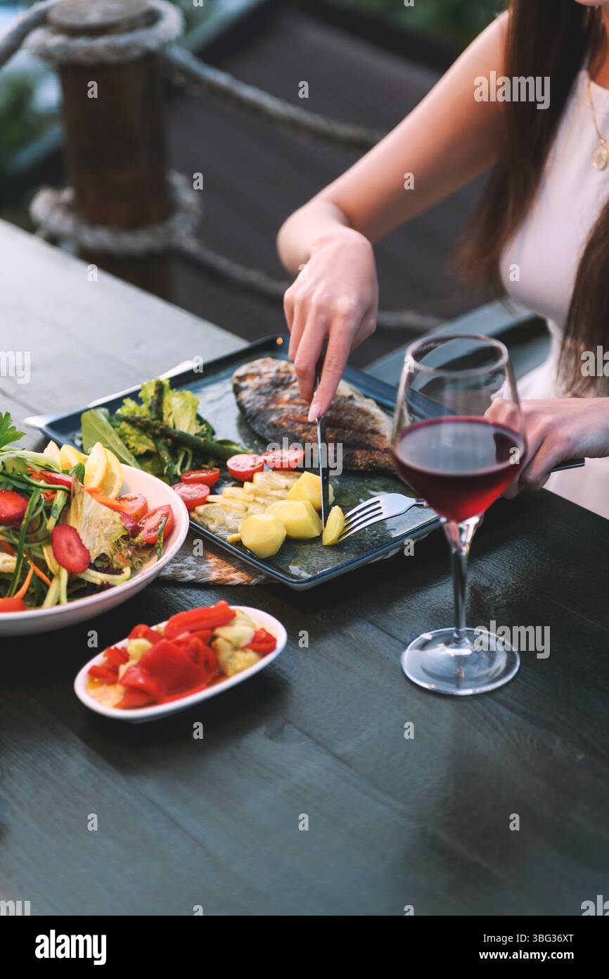 Uno scatto ravvicinato delle mani di una donna degli anni '20 che usa posate per tagliare pesce e patate in un ristorante di lusso. Foto Stock