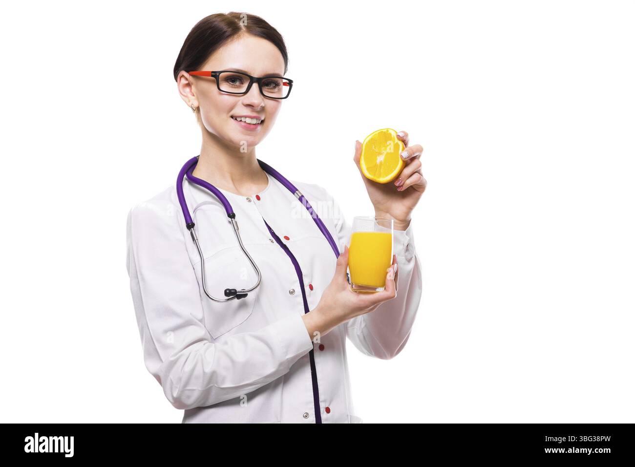 Ritratto della giovane bruna caucasica attraente donna sorridente positiva nutrizionista in piedi in ufficio con frutta mandarino arancio e vetro Foto Stock
