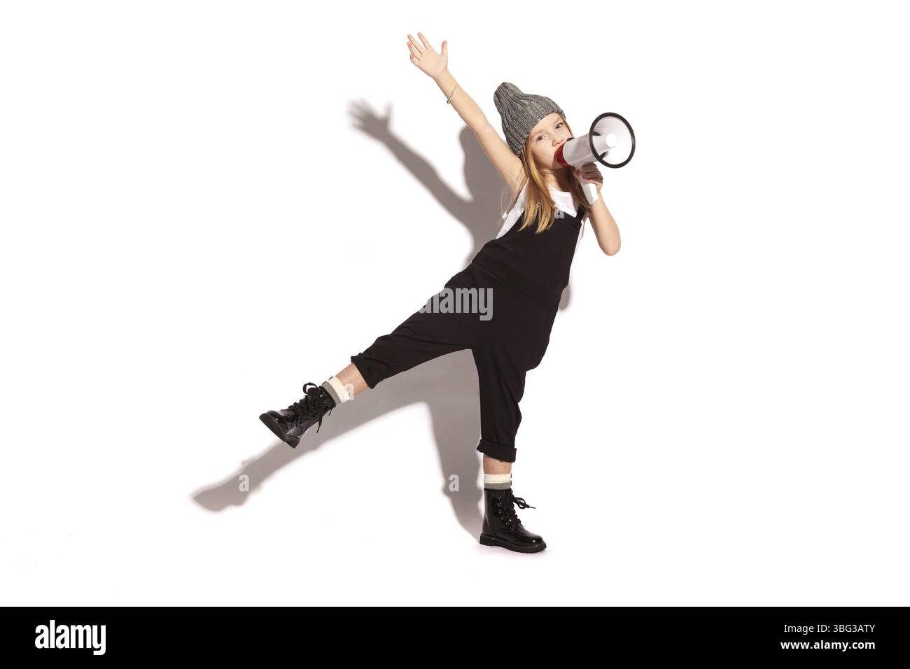 Isolata su una ragazza bianca dai capelli rossi, allegra e senza denti con tute nere, t-shirt bianca, cappello grigio e scarpe lacci laccate, che parla nella Foto Stock