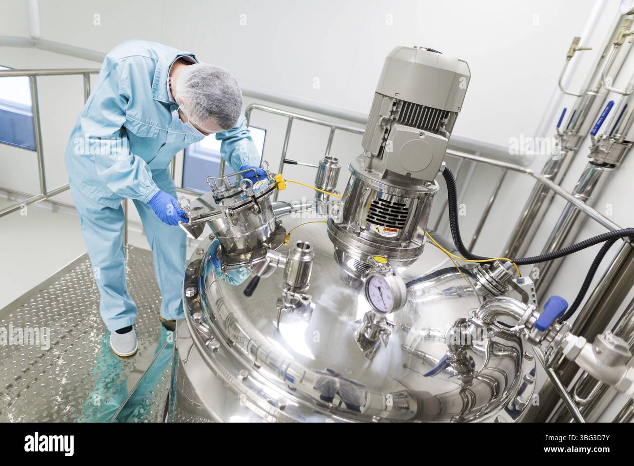 Scienziato piegato in tuta da laboratorio blu per lavorare con grandi serbatoi cromati Foto Stock