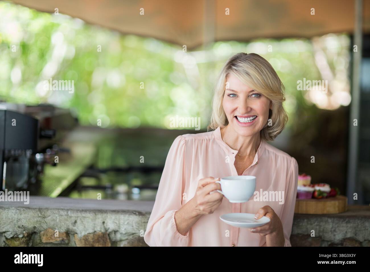 Donna di mezza età che indossa una tazza sorridente con la parte superiore rosa, piattino al bar con pasticcini, spazio per le copie Foto Stock