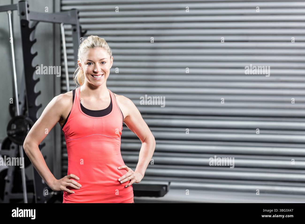 Donna in piedi con le mani sui fianchi in palestra accanto al portapacchi ponderato e alla porta a serranda Foto Stock