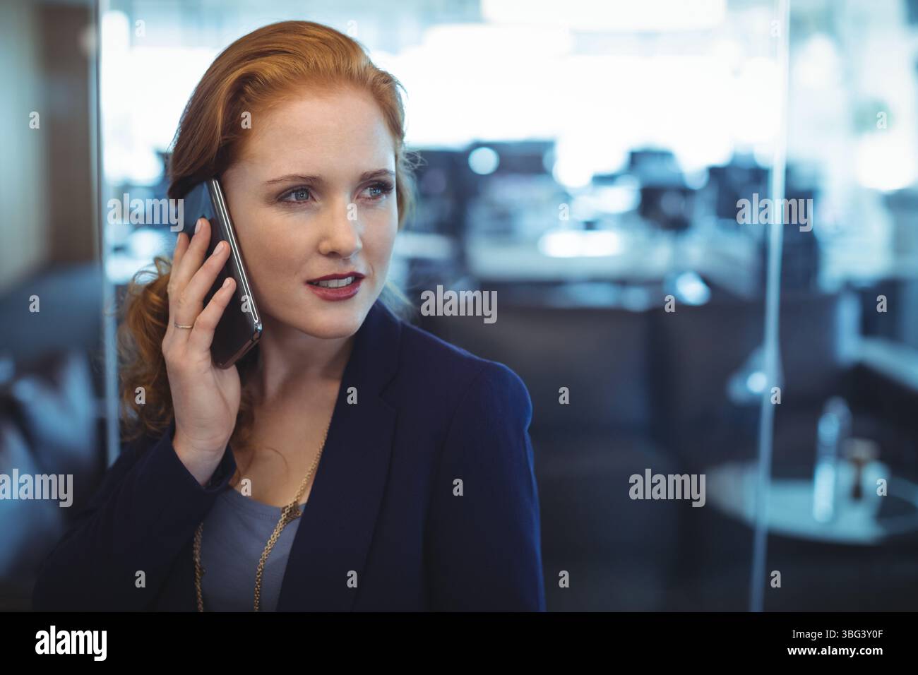 Donna in vestibilità formale in piedi nella sala d'ufficio che parla sullo smartphone con una partizione in vetro e uno spazio di copia Foto Stock