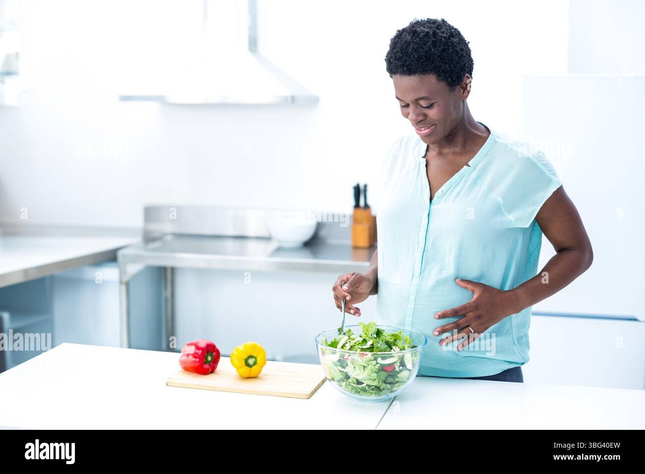 Donna afroamericana che mescola l'insalata verde in una ciotola sul bancone della cucina con peperoni, spazio copia Foto Stock