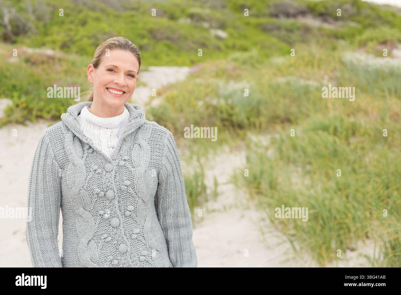 Donna anziana che indossa un cappotto grigio in maglia a cavo, un maglione in maglia in piedi sul percorso delle dune, copia spazio Foto Stock