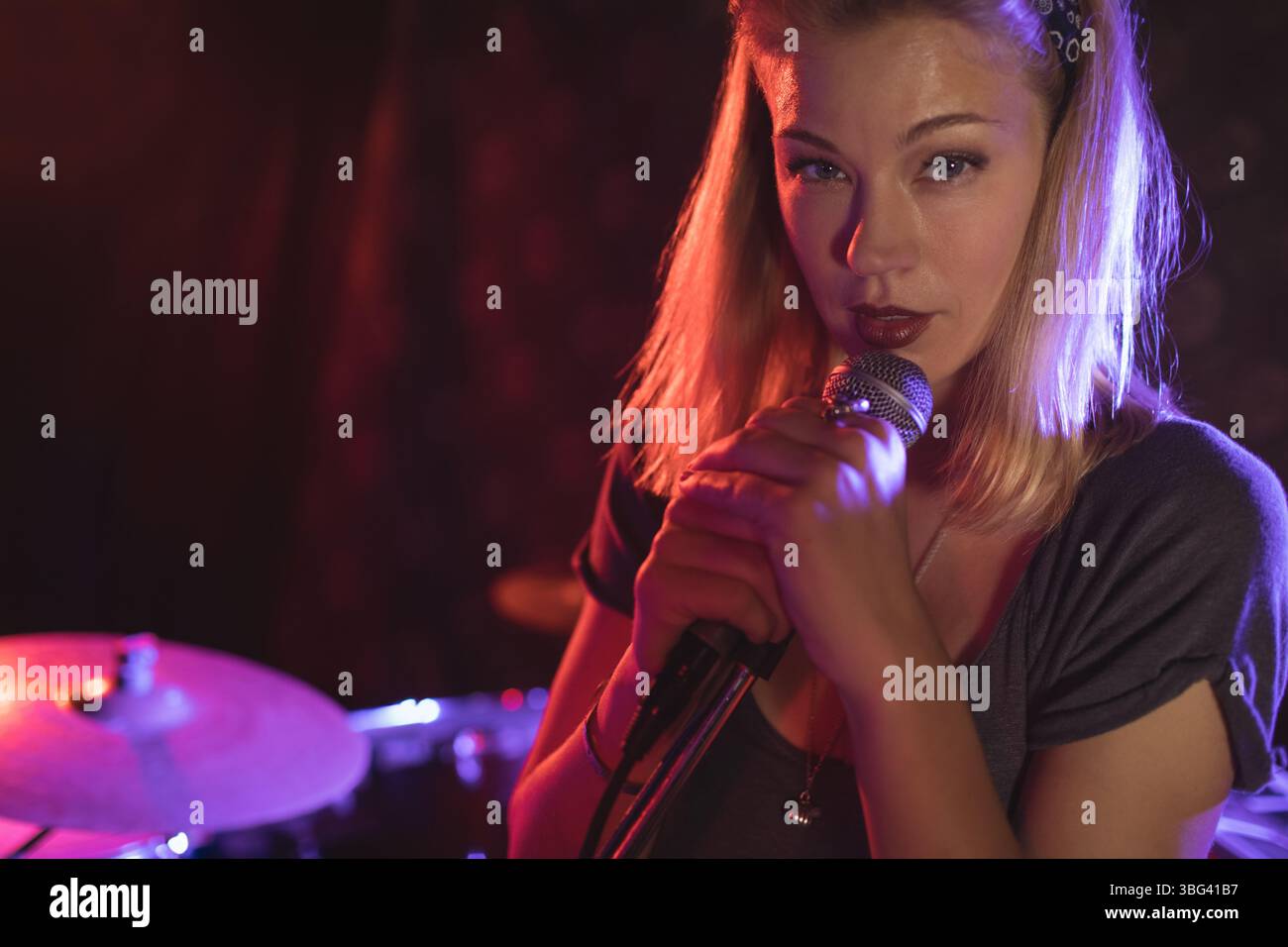 Cantante femminile che canta nel microfono sul palco del palco del palco con batteria sotto l'illuminazione del palco Foto Stock