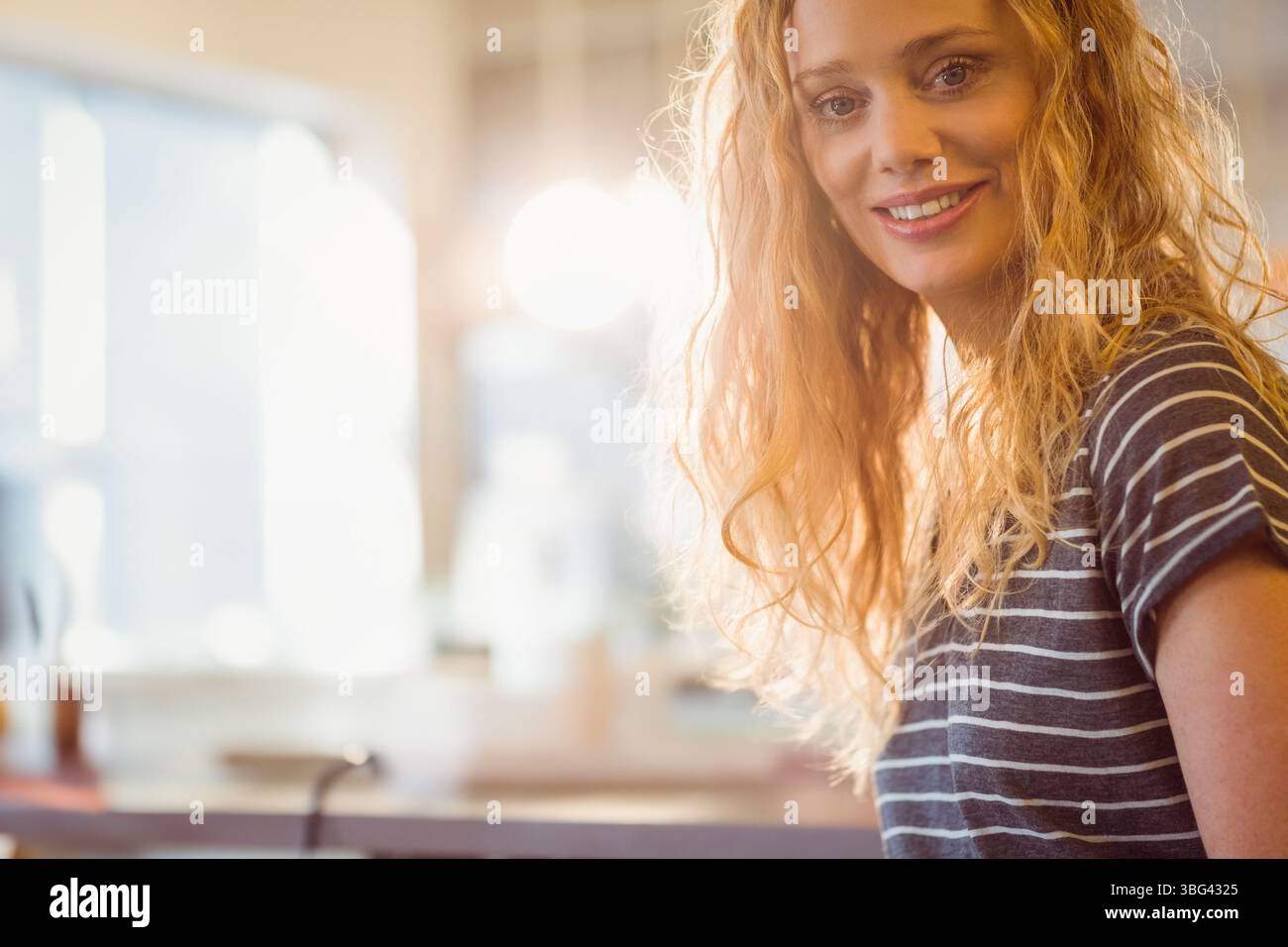 Donna adulta sorridente appoggiandosi al piano di lavoro della cucina con utensili e luce della finestra, spazio fotocopie Foto Stock