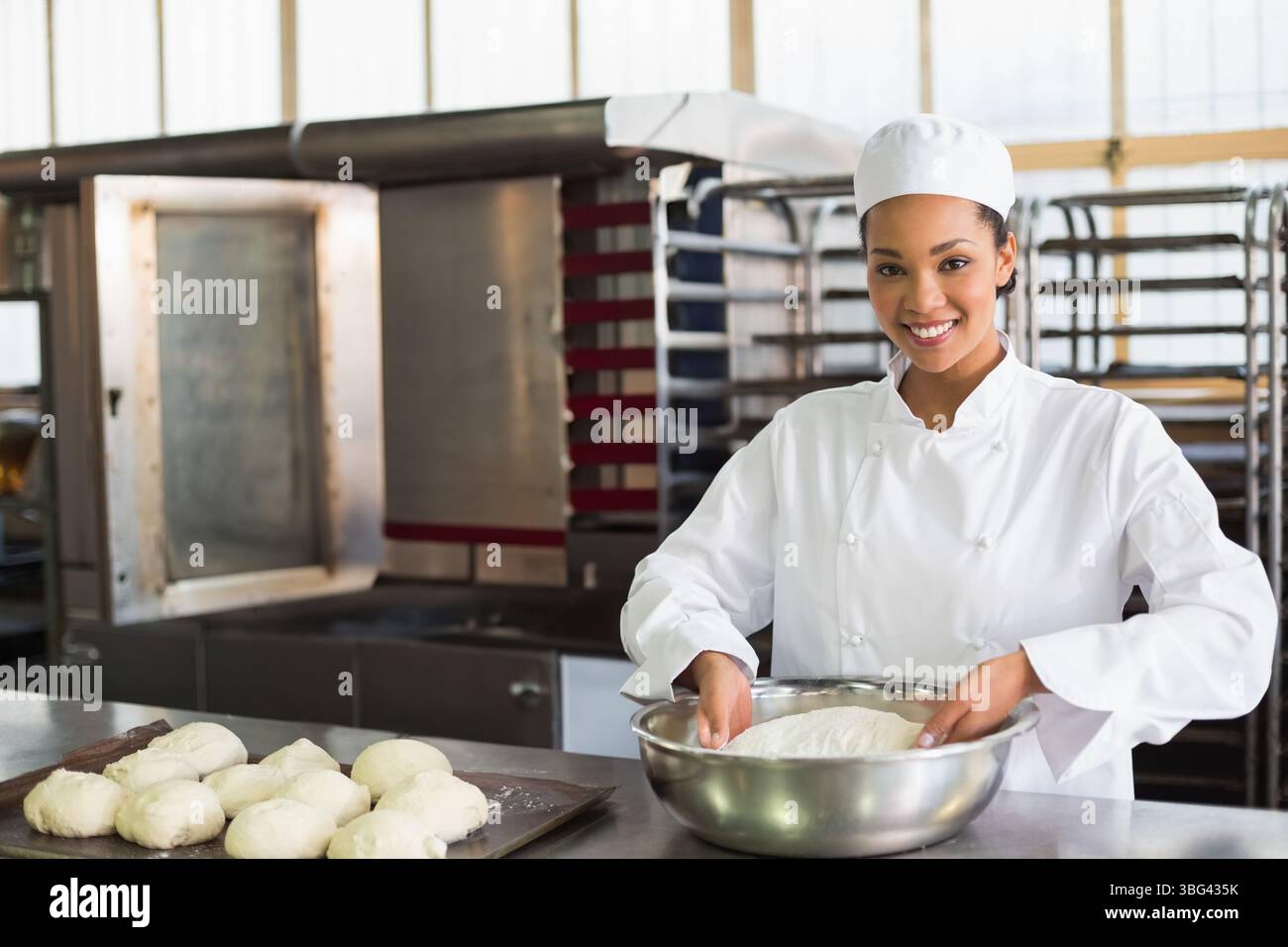 Donna afroamericana che indossa il cappotto dello chef impastando l'impasto con una ciotola per mescolare al forno, copia spazio Foto Stock