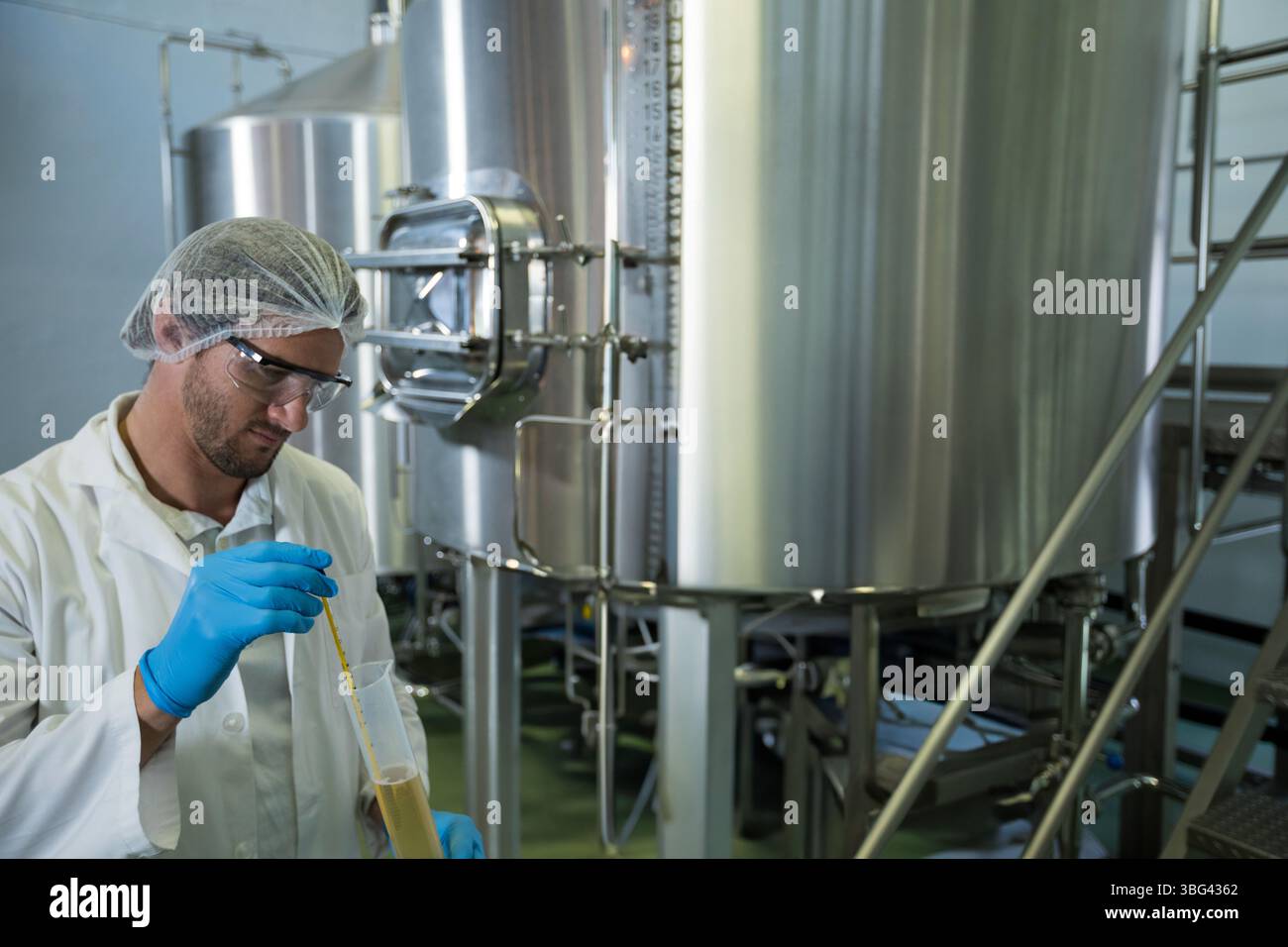 Il liquido giallastro viene aspirato in un cilindro graduato in vetro utilizzando una pipetta nel laboratorio di birreria con serbatoi Foto Stock