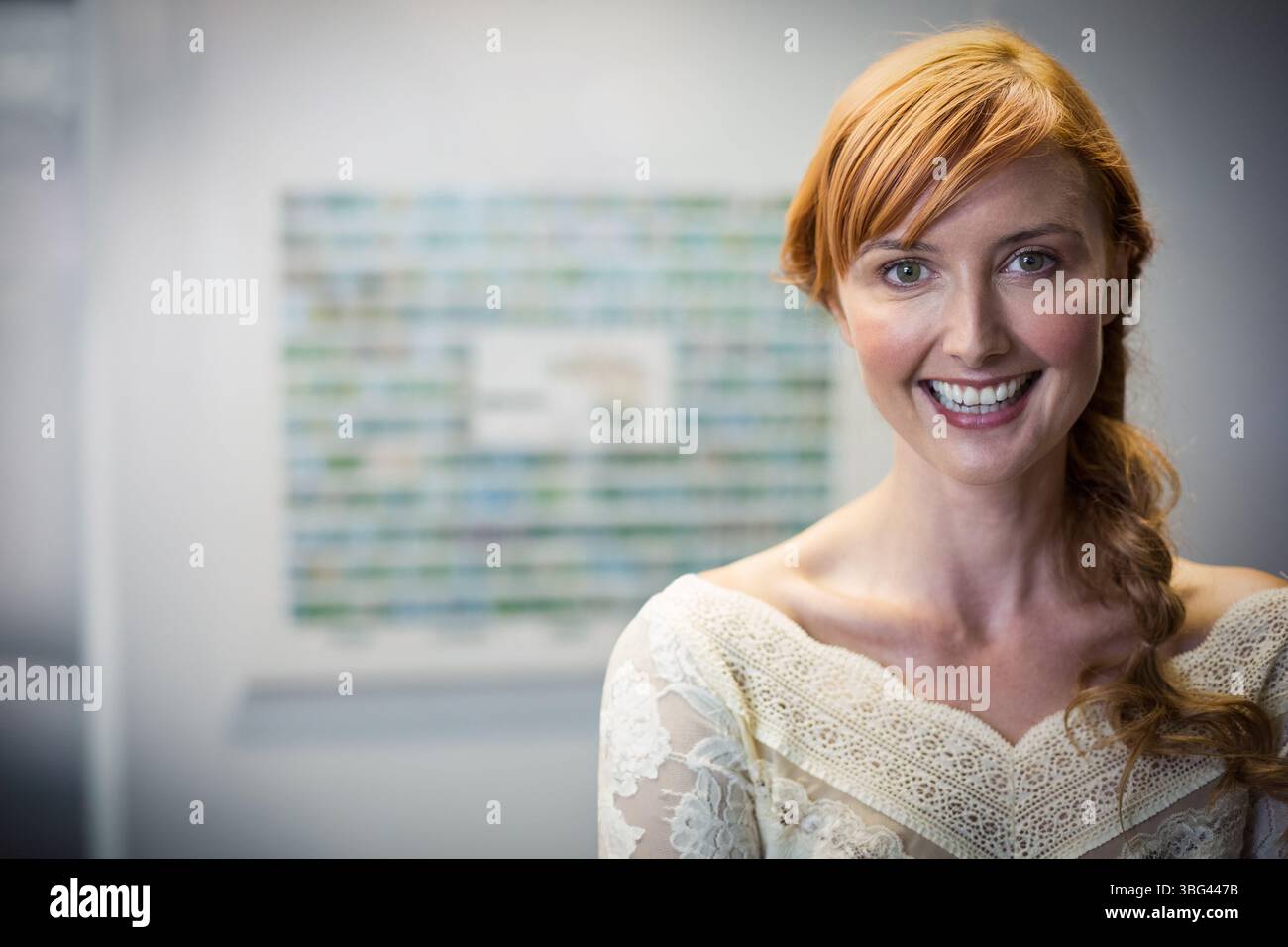 Donna dai capelli rossi che indossa la parte superiore in pizzo color crema, sorridente prima di opere d'arte sfocate nella galleria moderna Foto Stock