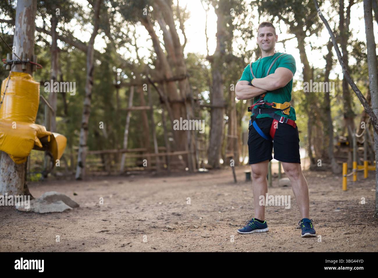 Uomo in piedi che indossa imbracature e moschettoni nel parco avventura forestale con scale a fune e spazio per copiare Foto Stock