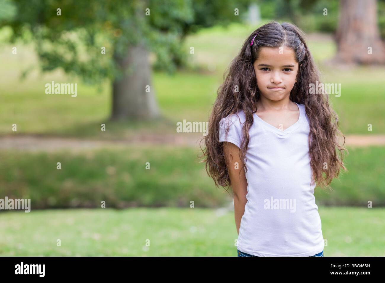 Ragazza in piedi in un parco pubblico ben tenuto con clip per capelli rosa nei capelli vicino all'albero, spazio fotocopie Foto Stock
