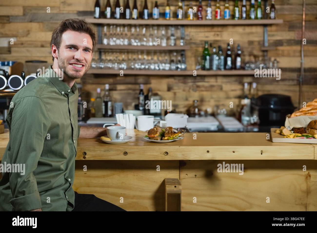 Un uomo seduto al bancone del bar che beve un caffè con piatto sandwich e agitatori, spazio per fotocopie Foto Stock