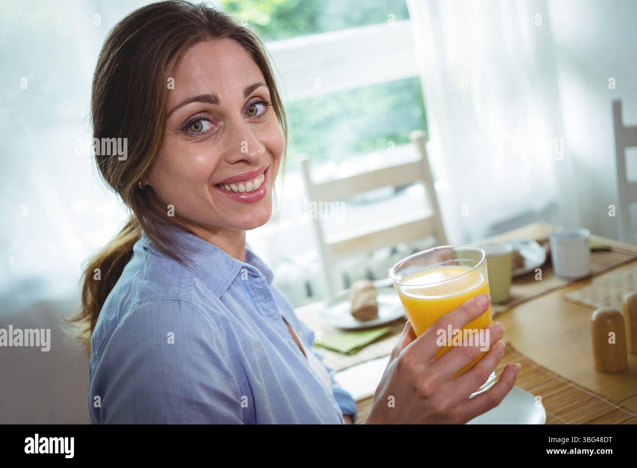 Donna degli anni '30 seduta al tavolo da pranzo tenendo un bicchiere di succo d'arancia vicino alla finestra, copia spazio Foto Stock