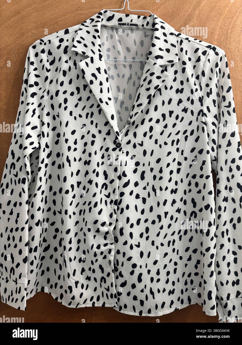 Camicetta da donna a maniche lunghe con macchie di mucca bianche e nere appesa su uno sfondo in legno. Foto Stock