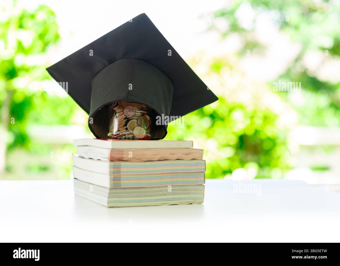 Un cappuccio graduato si trova sopra un vaso di monete, che viene posizionato su una pila di libri su sfondo sfocato. Foto Stock