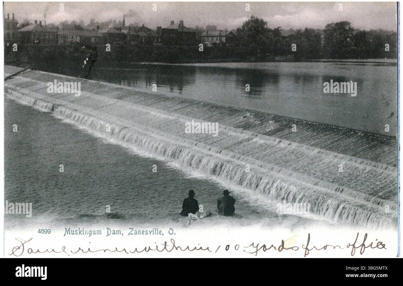 Questa foto in bianco e nero del 1905 raffigura la diga di Muskingum a Zanesville, Ohio, con due uomini seduti lungo la riva del fiume. Gli edifici sono visibili dall'altra parte del fiume. Foto Stock