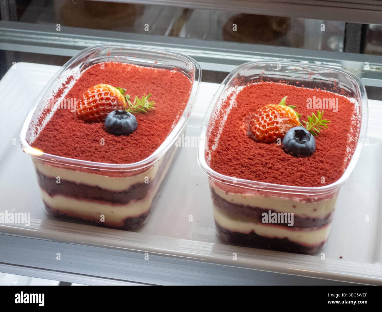 Due deliziosi strati di dessert in velluto rosso in tazze limpide, ricoperti di fragole e mirtilli, perfetti per qualsiasi festa o dolcezza cravin Foto Stock