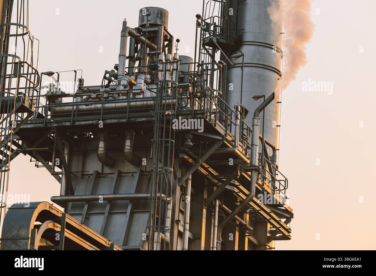 Il camino dell'edificio della centrale elettrica a turbina a gas rilascia vapore, mentre l'edificio ingegneristico si affaccia sullo sfondo del cielo del tramonto Foto Stock