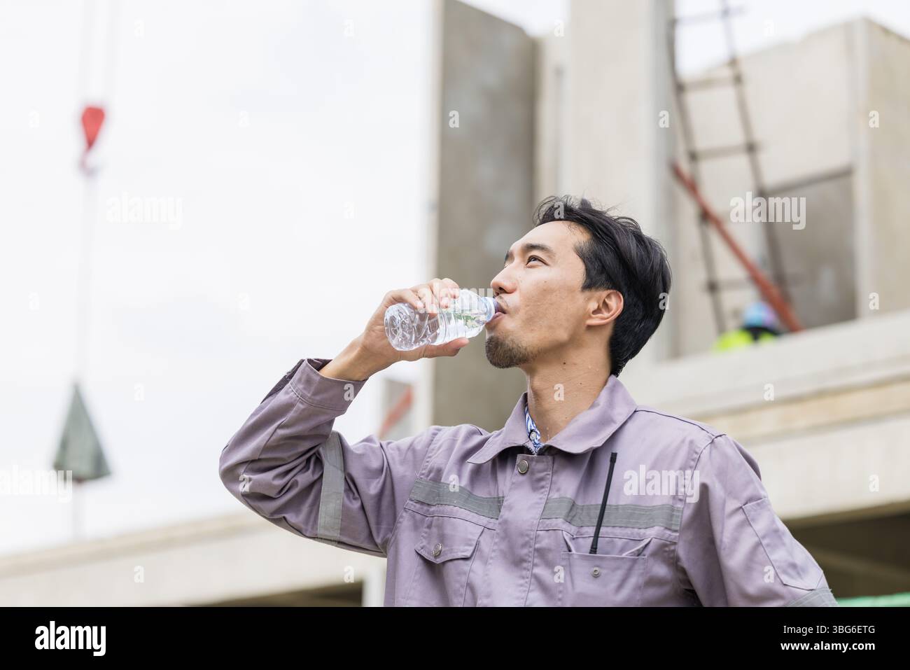 Uomo lavoratore asiatico sete di acqua potabile in estate calda lavorando all'aperto in cantiere Foto Stock