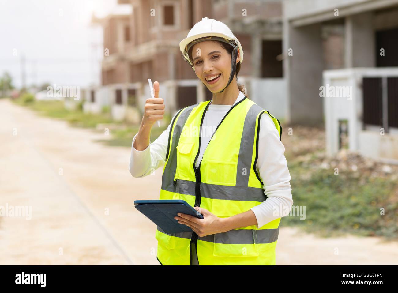 Donna felice ingegnere edile, donne intelligenti con gilet riflettente di sicurezza pollice sicuro sorridere in cantiere all'aperto. Foto Stock