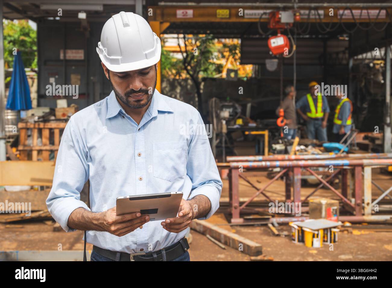 Ritratto ingegnere edile ispanico indiano lavoratore maschile in cantiere con elmetto di sicurezza che guarda il tablet computer Foto Stock