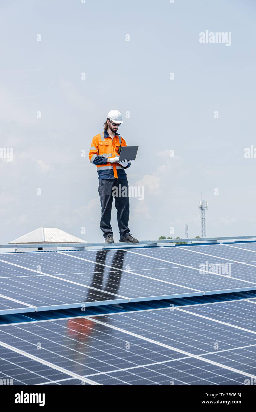 Lavoratori che installano pannelli solari sul tetto utilizzando il software del laptop, controllano lo stato della velocità di alimentazione Foto Stock