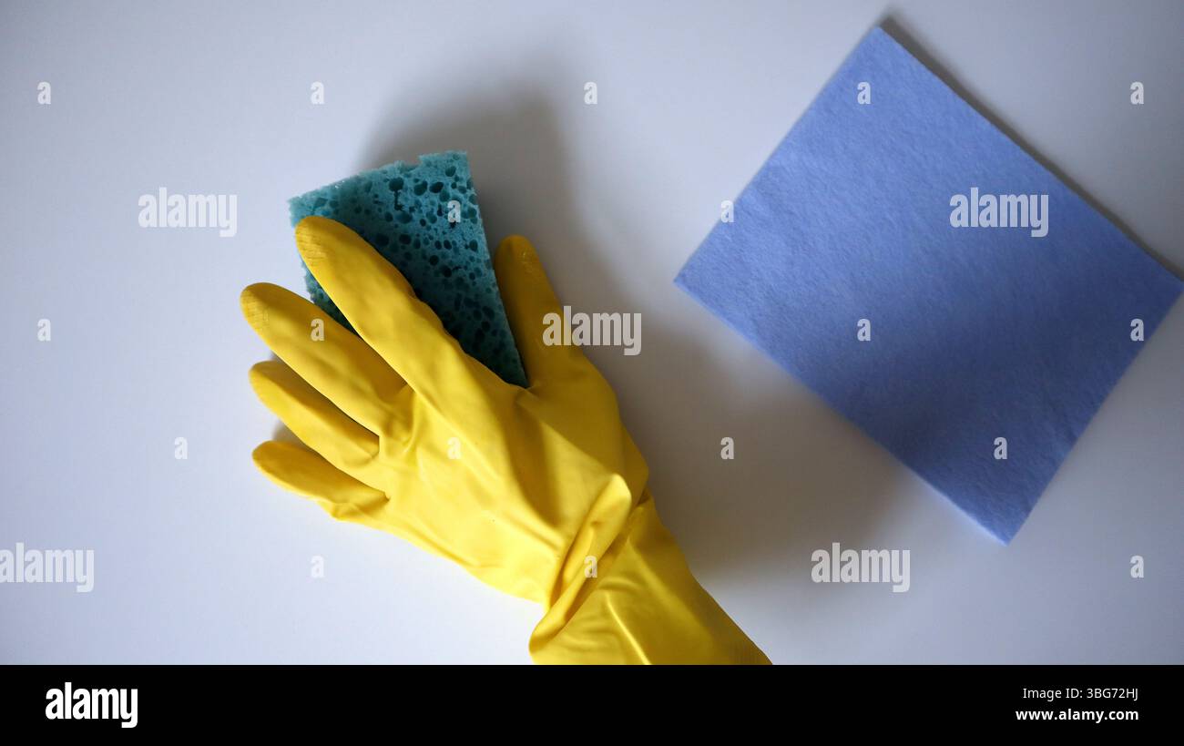 Fotografia del processo di pulizia, lavaggio della superficie. Una mano in un guanto di gomma pulisce il tavolo con una spugna. Nelle vicinanze è presente una spugna di cellulosa. Guanto giallo Foto Stock