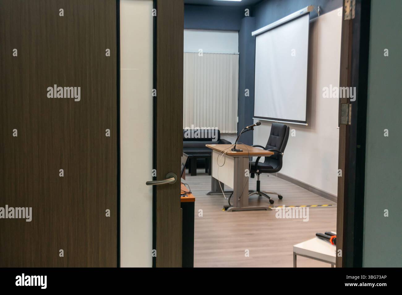 Una moderna sala conferenze con porta aperta, dotata di tavolo e sedia eleganti, schermo proiettore e design minimalista, ideale per riunioni o presentazioni Foto Stock