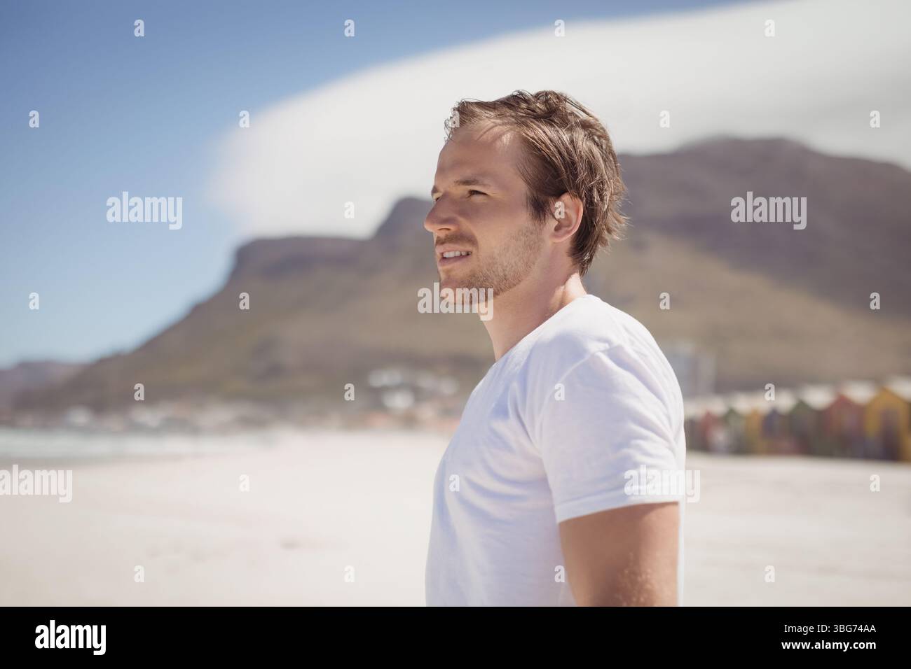 Uomo che indossa una T-shirt bianca che guarda l'orizzonte sulla spiaggia con capanne sulla spiaggia, spazio copia Foto Stock