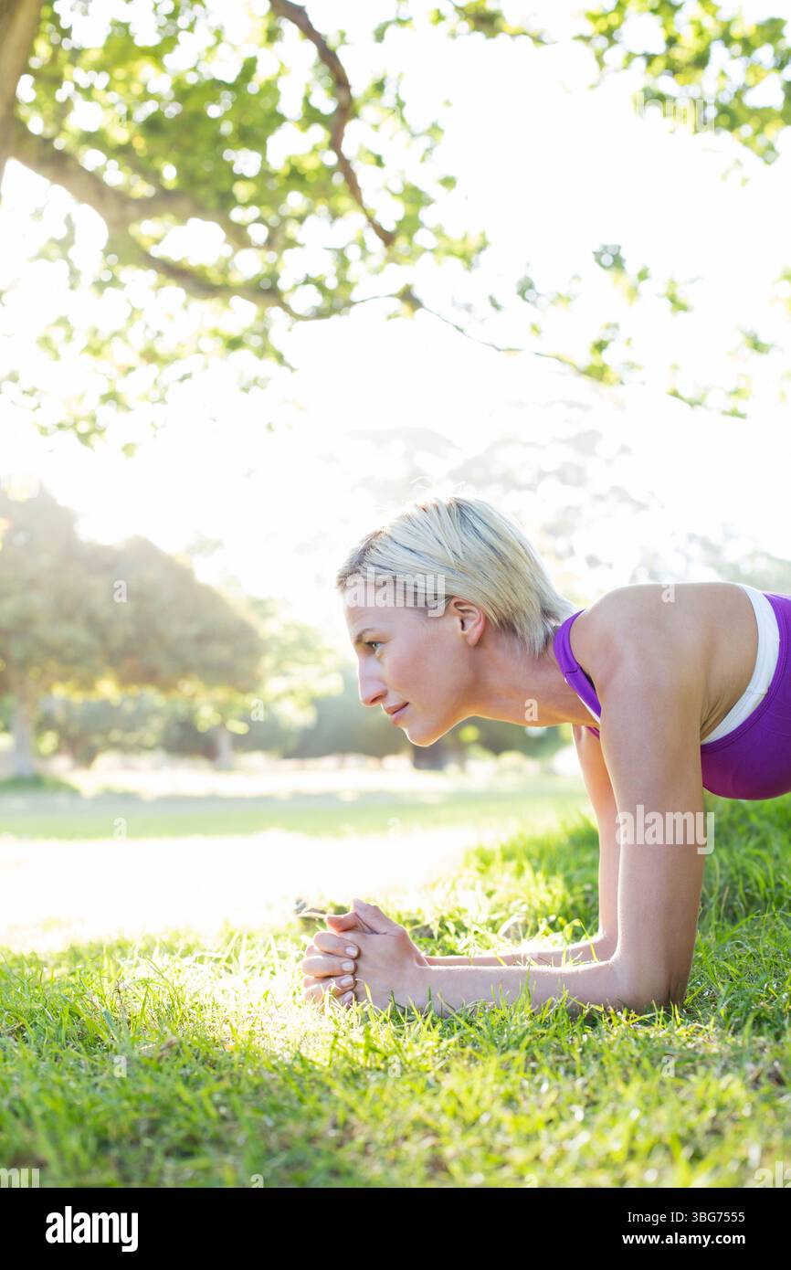 donna che tiene la tavola e indossa un abbigliamento atletico sul prato del parco sotto gli alberi, spazio fotocopie Foto Stock