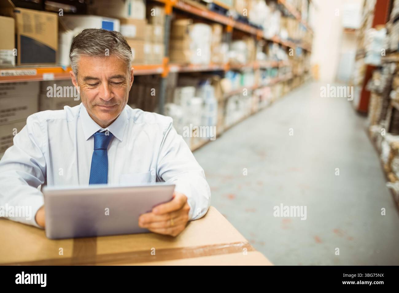 Uomo in camicia e cravatta che controlla l'inventario sul tablet appoggiato alle scatole in magazzino, copia spazio Foto Stock