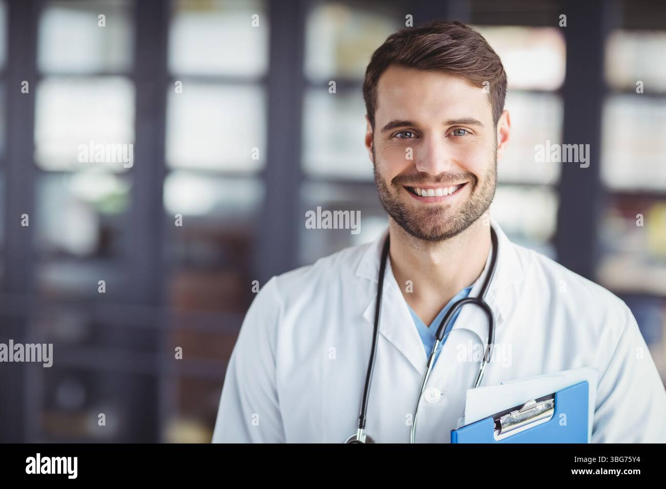 Il medico è in piedi e sorride nella reception della clinica, tenendo gli appunti e indossando lo stetoscopio Foto Stock