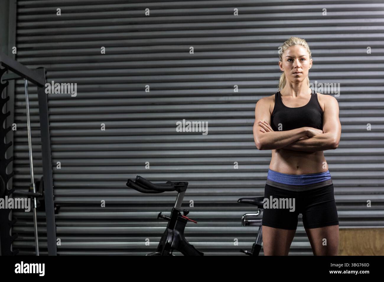 Atleta in piedi con le braccia incrociate in palestra con otturatore metallico, bicicletta, portapacchi, spazio per copiare Foto Stock