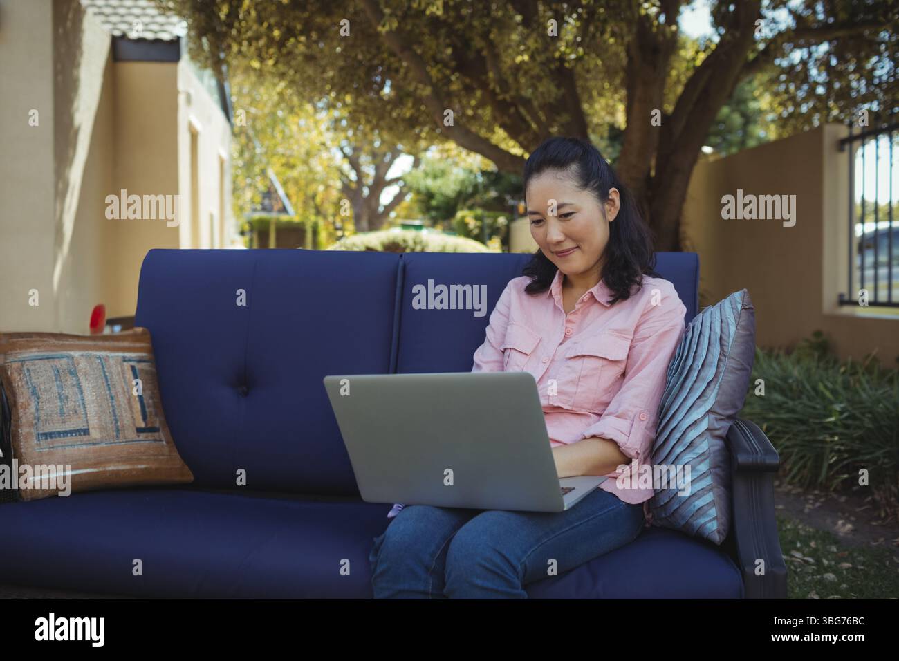 Donna coreana adulta matura seduta su un divano blu con laptop grigio argento con cuscini e spazio per fotocopie Foto Stock