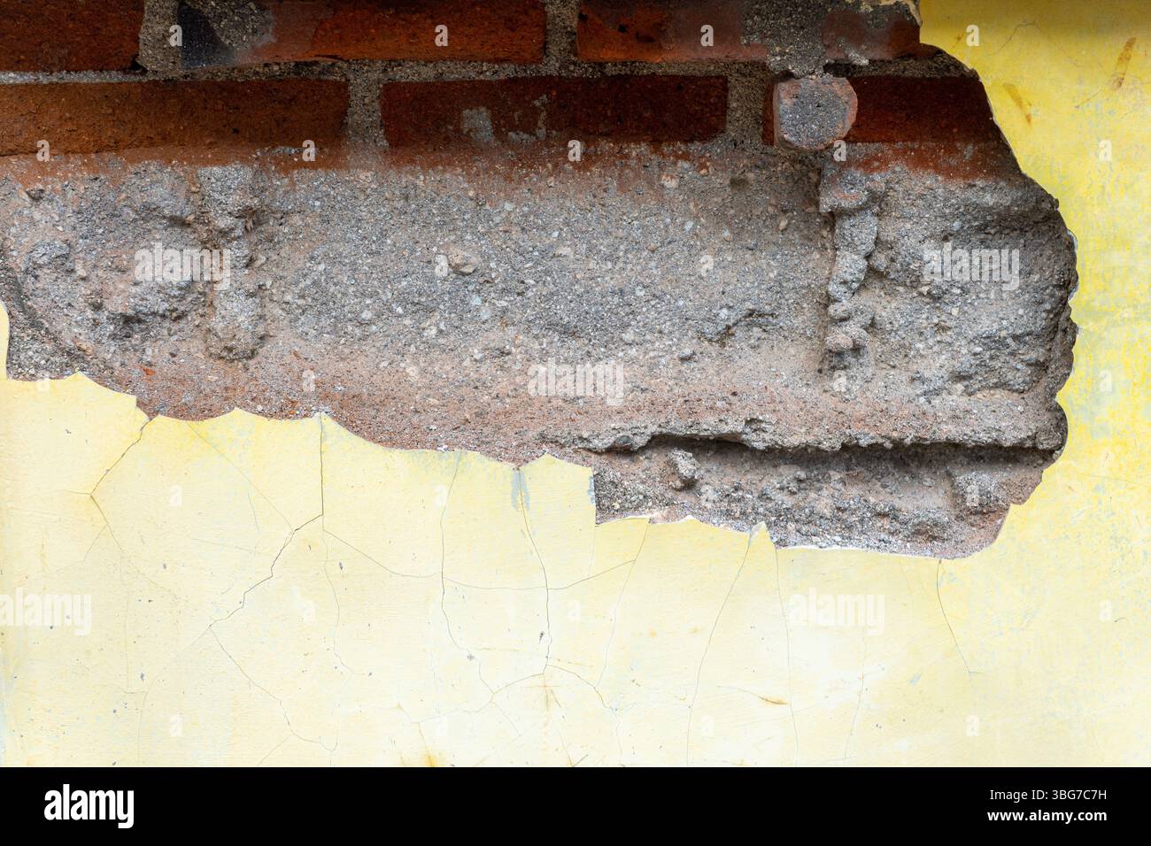 Muro con un foro e una vernice gialla e bianca. Il muro è fatto di mattoni Foto Stock