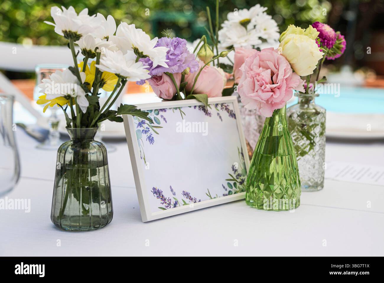 Elegante disposizione del tavolo con una cornice bianca in mockup circondata da piccoli vasi di colorati fiori primaverili. Perfetto per inviti di nozze, eventi ann Foto Stock