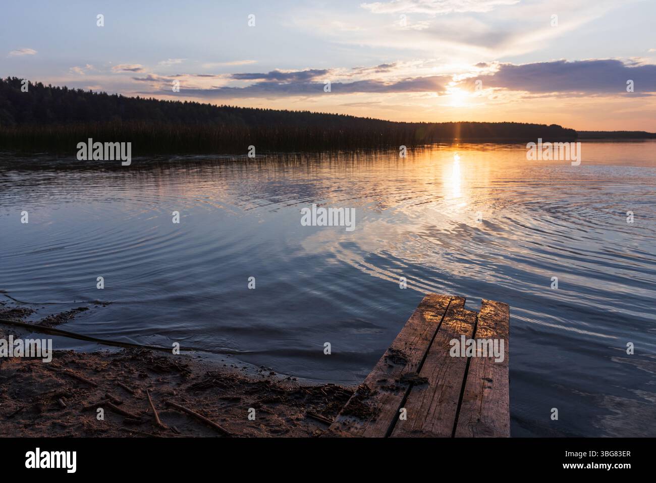 Splendido tramonto su un lago tranquillo, caratterizzato da un molo in legno e da tranquilli riflessi d'acqua. Lo sfondo boscoso aggiunge un'atmosfera naturale e rilassante, pe Foto Stock