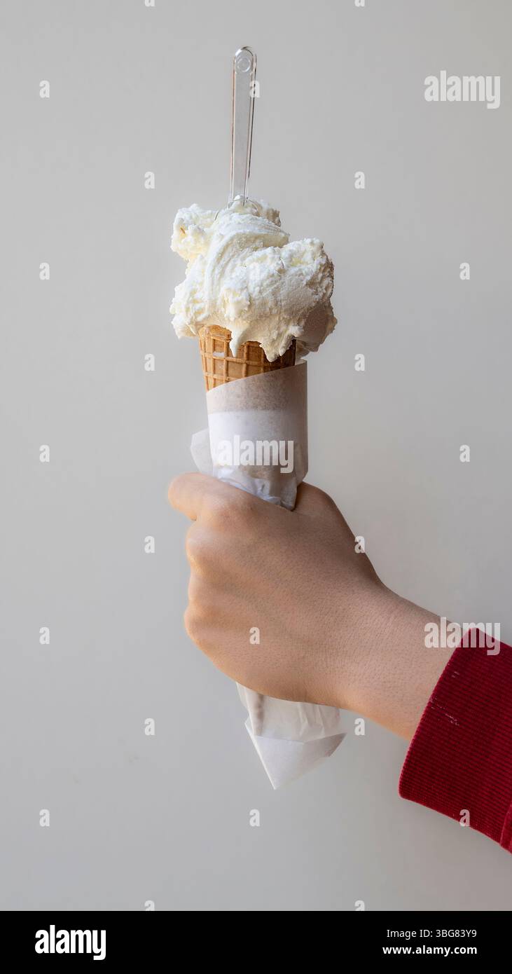Tenere a mano un delizioso cono per waffle con cucchiai di cremosa vaniglia bianca o gelato al cocco. Un dessert congelato rinfrescante perfetto per una calda estate Foto Stock