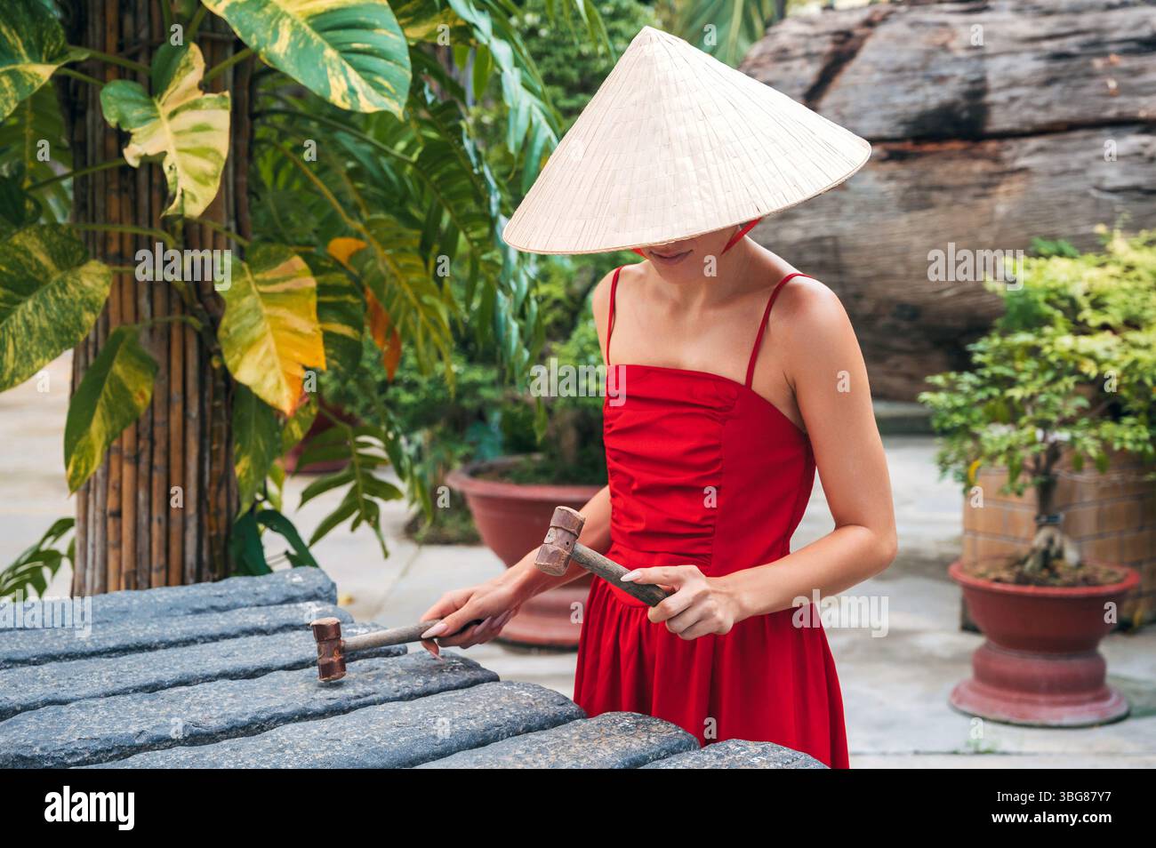 Donna asiatica con un cappello conico che gioca su Dan da o litofono. Strumento musicale tradizionale vietnamita. Foto Stock