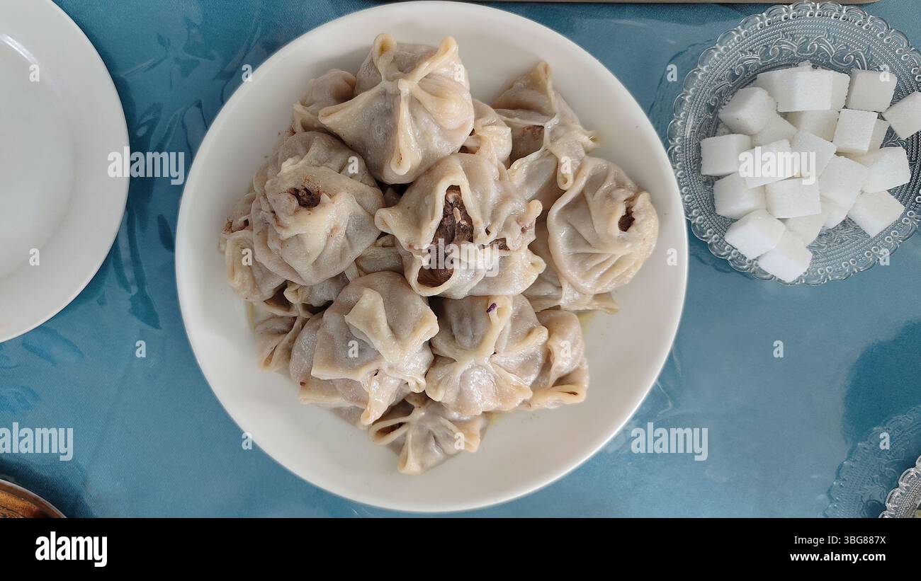 Gnocchi mongoli al vapore, noti come buuz, serviti su un piatto bianco, accompagnati da un piccolo piatto a cubetti di zucchero, che mostra la tradizione mongola Foto Stock