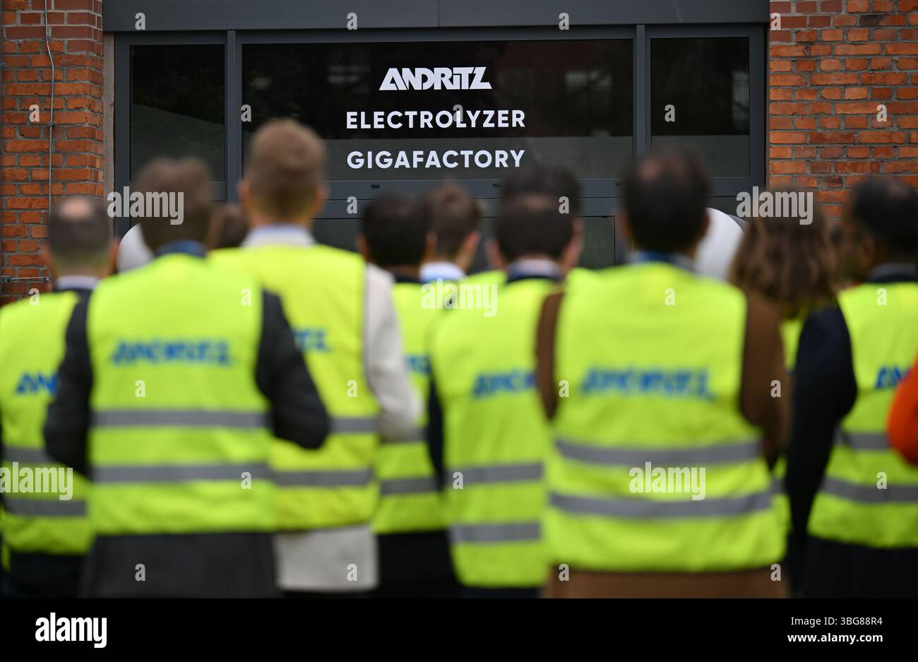 Erfurt, Germania. 4 giugno 2025. Gli ospiti dell'inaugurazione di un centro di competenza sull'elettrolisi di Andritz Schuler GmbH indossano giubbotti di sicurezza. Un impianto all'avanguardia per l'assemblaggio di pile di elettrolizzatori è stato costruito nel sito industriale di Erfurt, vecchio di oltre 100 anni. Gli elettrolizzatori sono di importanza cruciale per la produzione di idrogeno verde. Crediti: Martin Schutt/dpa/Alamy Live News Foto Stock