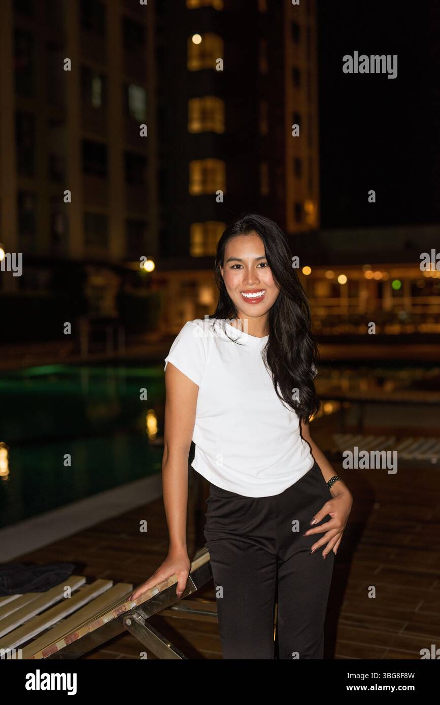 Ritratto di una giovane modella asiatica in posa accanto alla piscina durante la notte Foto Stock