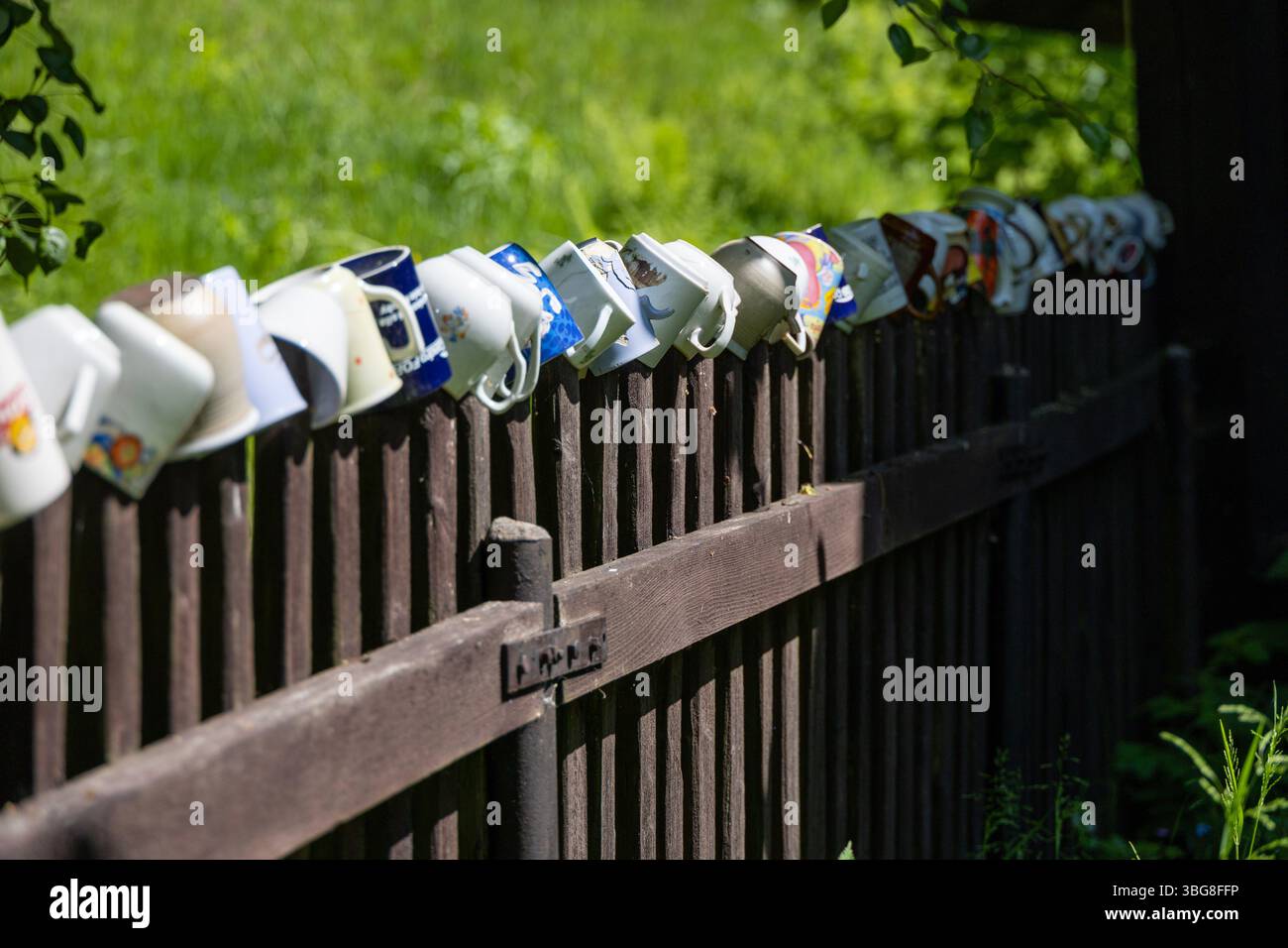 Collezione di tazze d'epoca colorate che decorano una recinzione in legno in un soleggiato giardino di campagna Foto Stock