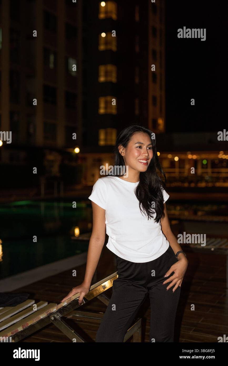 Ritratto di una giovane modella asiatica in posa accanto alla piscina durante la notte Foto Stock