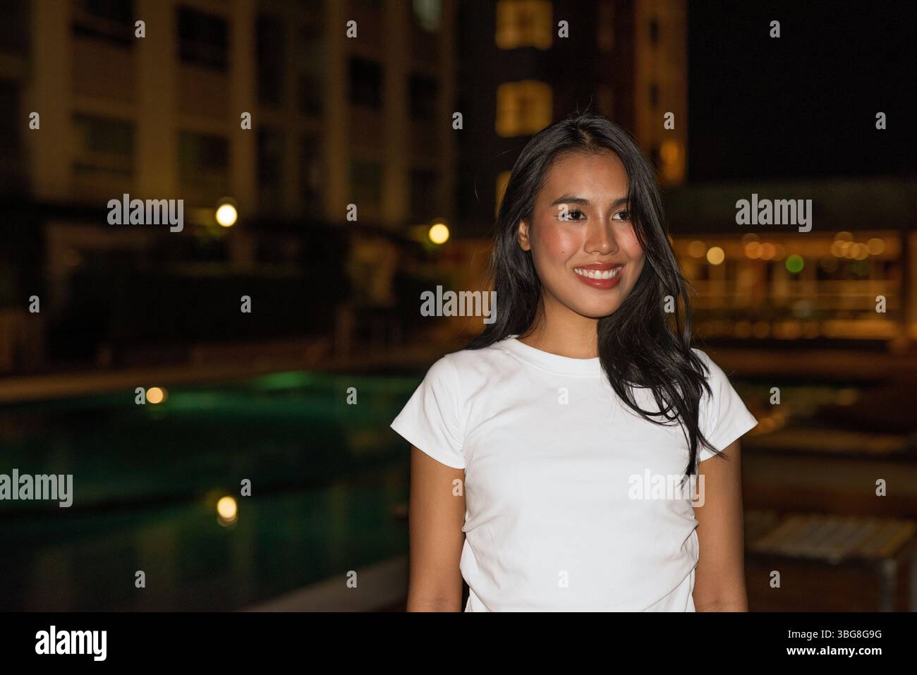 Ritratto di una giovane modella asiatica in posa accanto alla piscina durante la notte Foto Stock