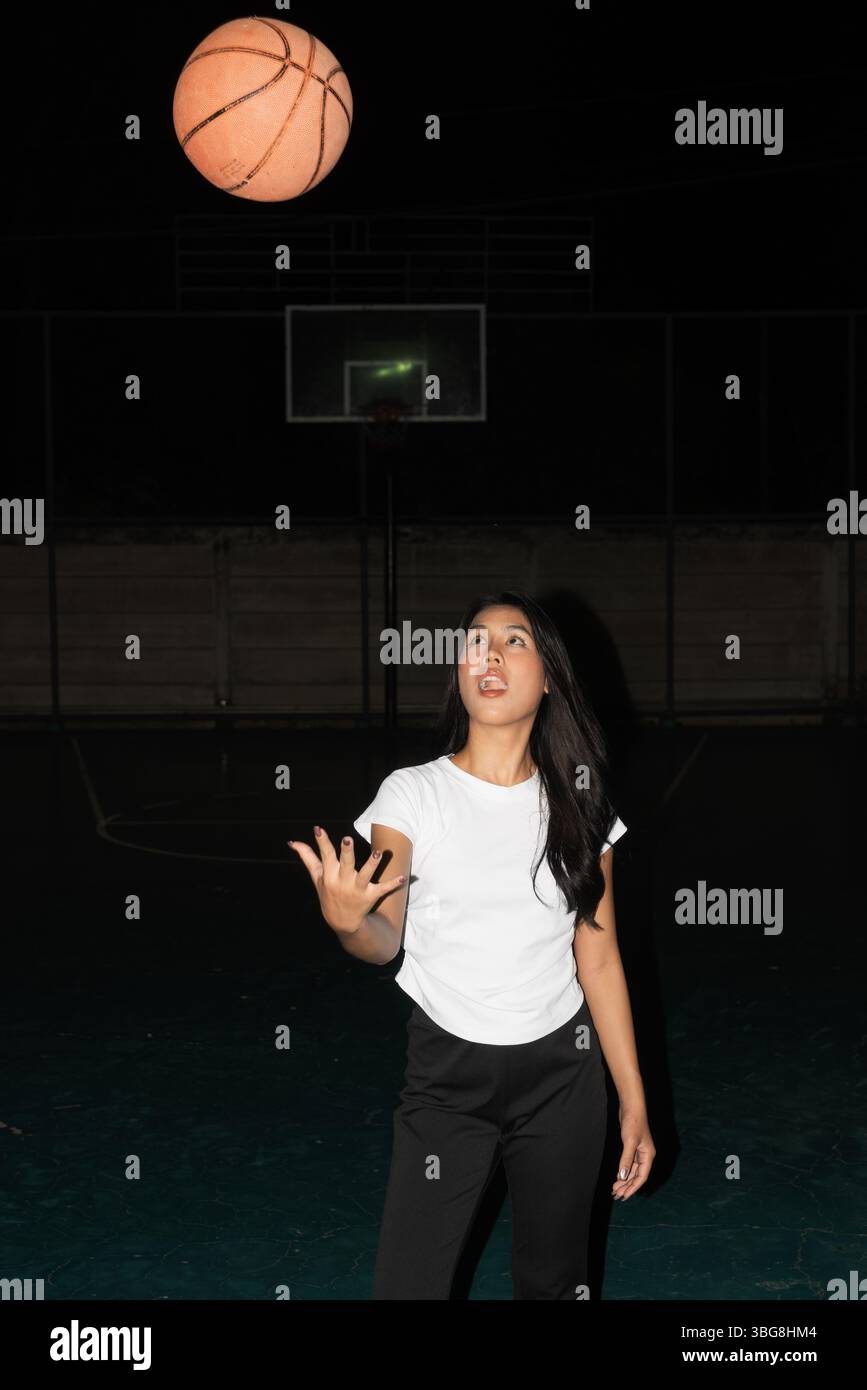 Giovane bella donna di notte nel campo da basket in posa Foto Stock