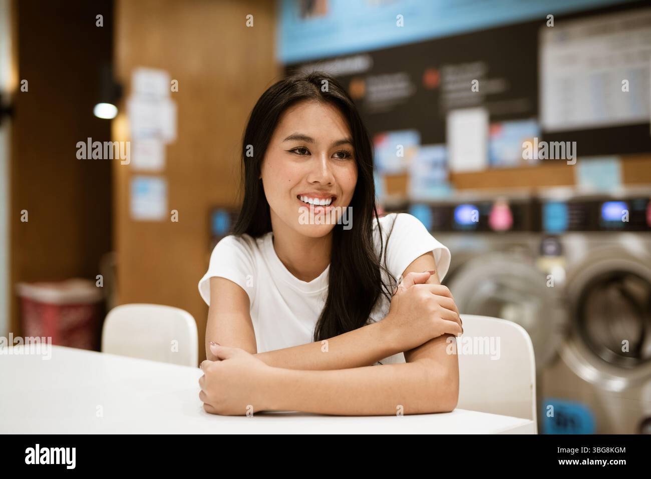 Giovane donna seduta in un negozio di lavanderia che fa lavori di casa Foto Stock