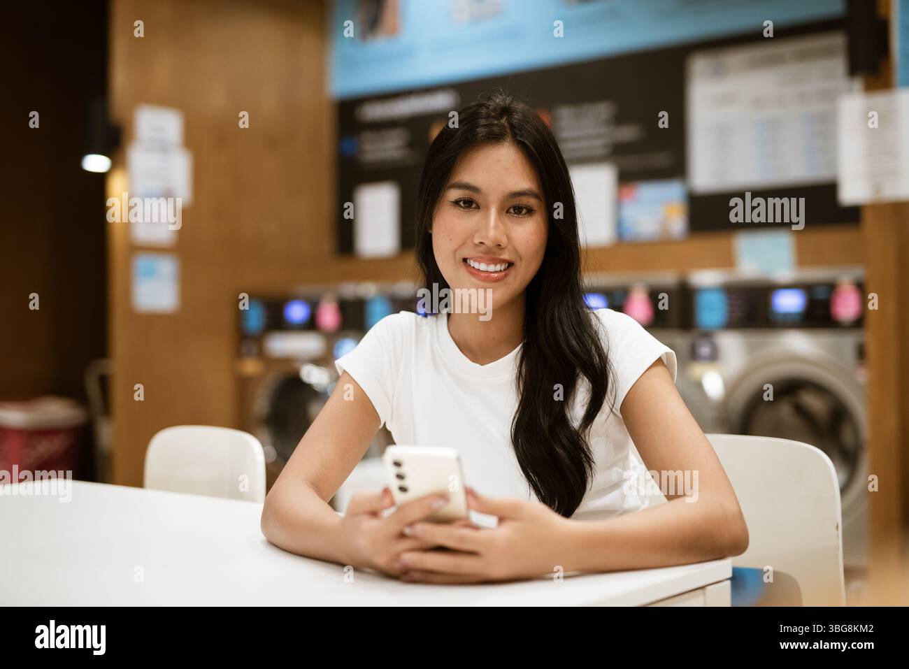 Giovane donna seduta in un negozio di lavanderia che fa lavori di casa Foto Stock