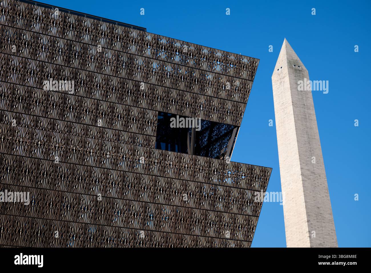 WASHINGTON DC - lo Smithsonian National Museum of African American History and Culture si erge in primo piano con il Washington Monument sullo sfondo del National Mall. Il caratteristico esterno in metallo color bronzo del museo, progettato dall'architetto David Adjaye e inaugurato nel settembre 2016, crea un contrasto sorprendente con l'obelisco in marmo bianco in onore del primo presidente americano. Questa vista cattura il dialogo architettonico tra il più recente museo Smithsonian della nazione e uno dei suoi monumenti più antichi. Foto Stock